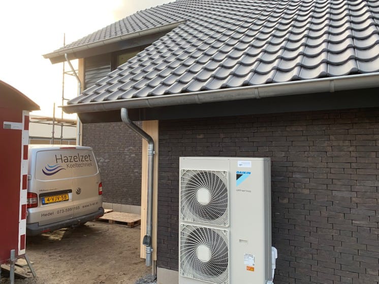 Daikin Altherma buitenunit geplaatst door Hazelzet Koeltechniek bij een moderne woning met donkere bakstenen gevel en een bedrijfswagen op de achtergrond.